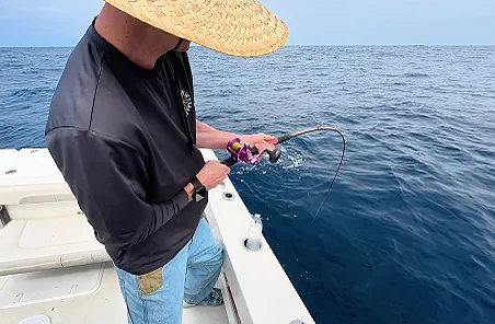 Angler in a straw hat fighting a fish beside the boat